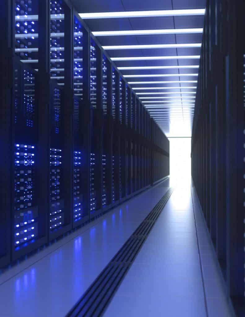 A corridor in a data center between two rows of server racks emitting a blue glow.