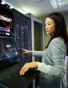 A woman uses a laptop in a server room.