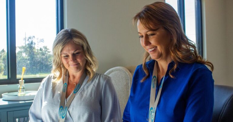 Two women wearing Alluvionic lanyards smile as they look at something out of frame.