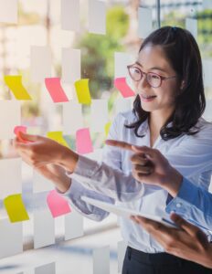 A woman with braces smiles as she adds a pink post-it note to a glass window covered in pink and yellow post-its.