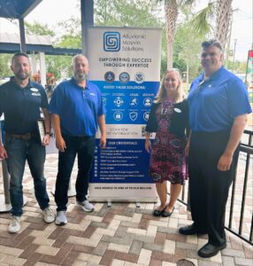 Four people stand in front of an Alluvionic Mayven Solutions banner smiling.