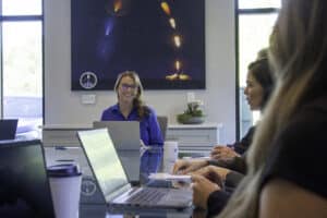 A woman in a blue shirt smiles over her computer at her coworkers.