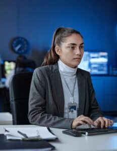 A woman in a white turtleneck and gray blazer types on a keyboard.