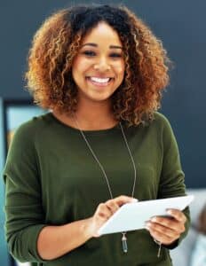 A woman in a green sweater smiles while using a tablet.