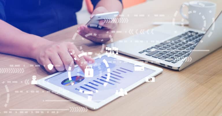 Person using a smartphone and tablet with a laptop on the desk, overlaid with digital icons representing data security, connectivity, and analytics.