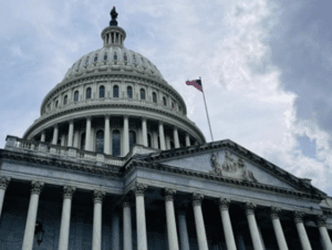 U.S. Capitol Building with the American flag flying on a cloudy day.