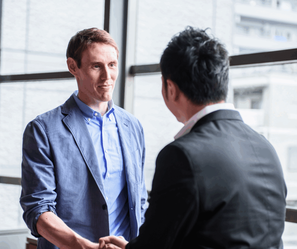 Two businessmen shaking hands in front of a large window that overlooks a city.