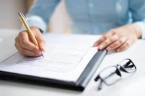 A person in a light blue shirt is writing on a clipboard with a pen. 