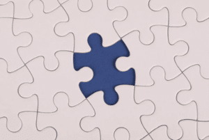 A white jigsaw puzzle is nearly complete, missing one piece. The empty space reveals a contrasting deep blue background, conveying a sense of incompleteness.