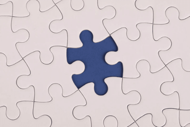 A white jigsaw puzzle is nearly complete, missing one piece. The empty space reveals a contrasting deep blue background, conveying a sense of incompleteness.