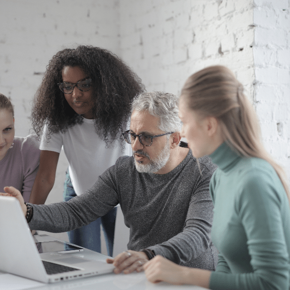 A group of professionals looking over a laptop and discussing amongst themselves.