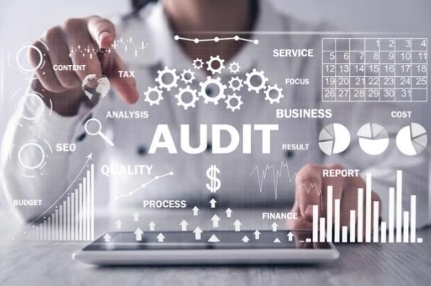 A person sitting at a grey desk with a tablet open on the surface overlayed with a white graphic that says Audit