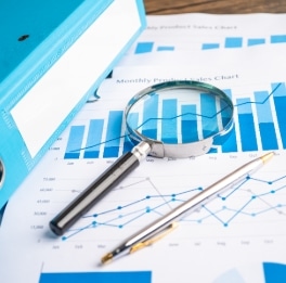 A magnifying glass and pen sitting on a data sheet with a binder sitting next to it on a table.